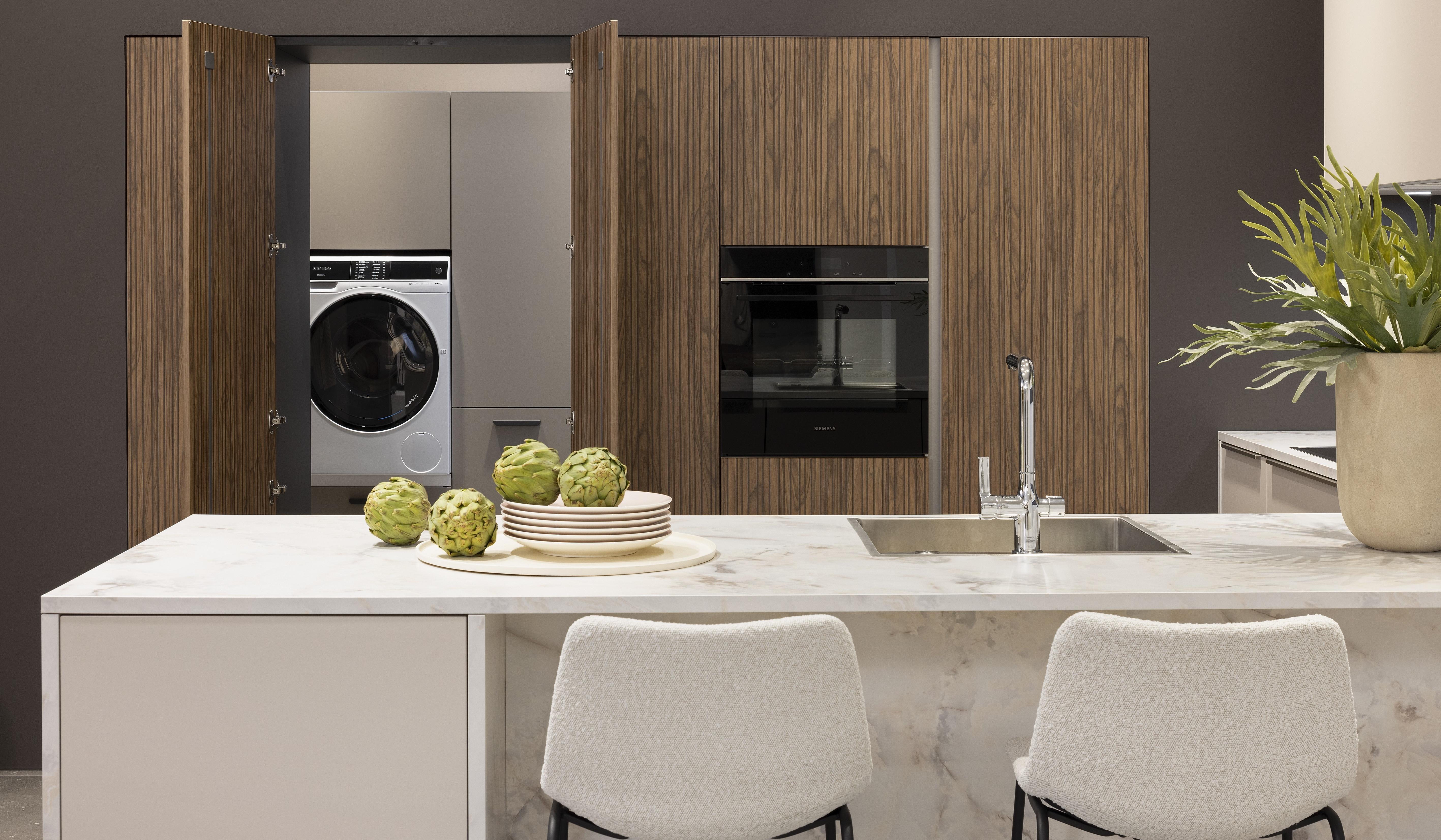 APL: Marmor Bianco 25 mm NB Front: Feel Sahara softmatt Front: WArtline Stripe Wood Choco Korpus: Sahara und Graphit Griff: Kehlleiste Edelstahloptik, und Griffe Edelstahloptik Geräte: Siemens  Armatur: Reginox Spüle: Reginox   Features: eingekoffertes Schrankelement, Tür zum HWR in Frontmaterial, niederer Sockel, Hängeoberschränke asymmetrisch mit Dunstabzug (als Esse geplant), Ecklösung mit LeMans Auszug, Theke mit Essplatz, Ordnungssystem Holz in Auszügen, Downlight in Arbeitsplatzbeleuchtung 